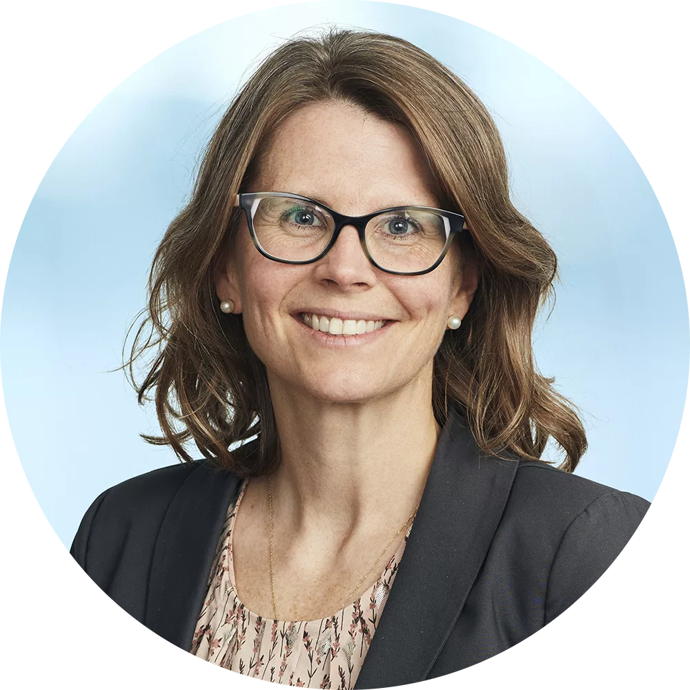 Karina Thorn wearing black rimmed glasses and a black blazer smiling nicely